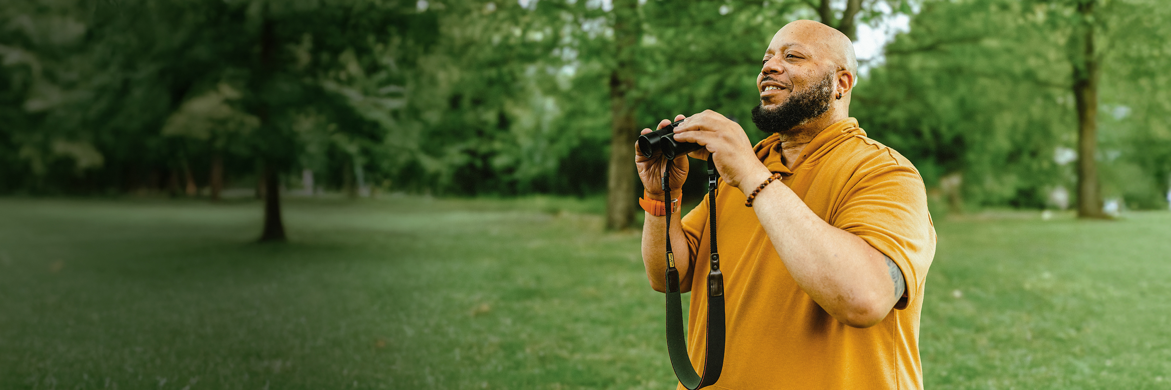 PYLARIFY Patient Al Outside Al, a PYLARIFY patient, standing outside in nature, holding binoculars