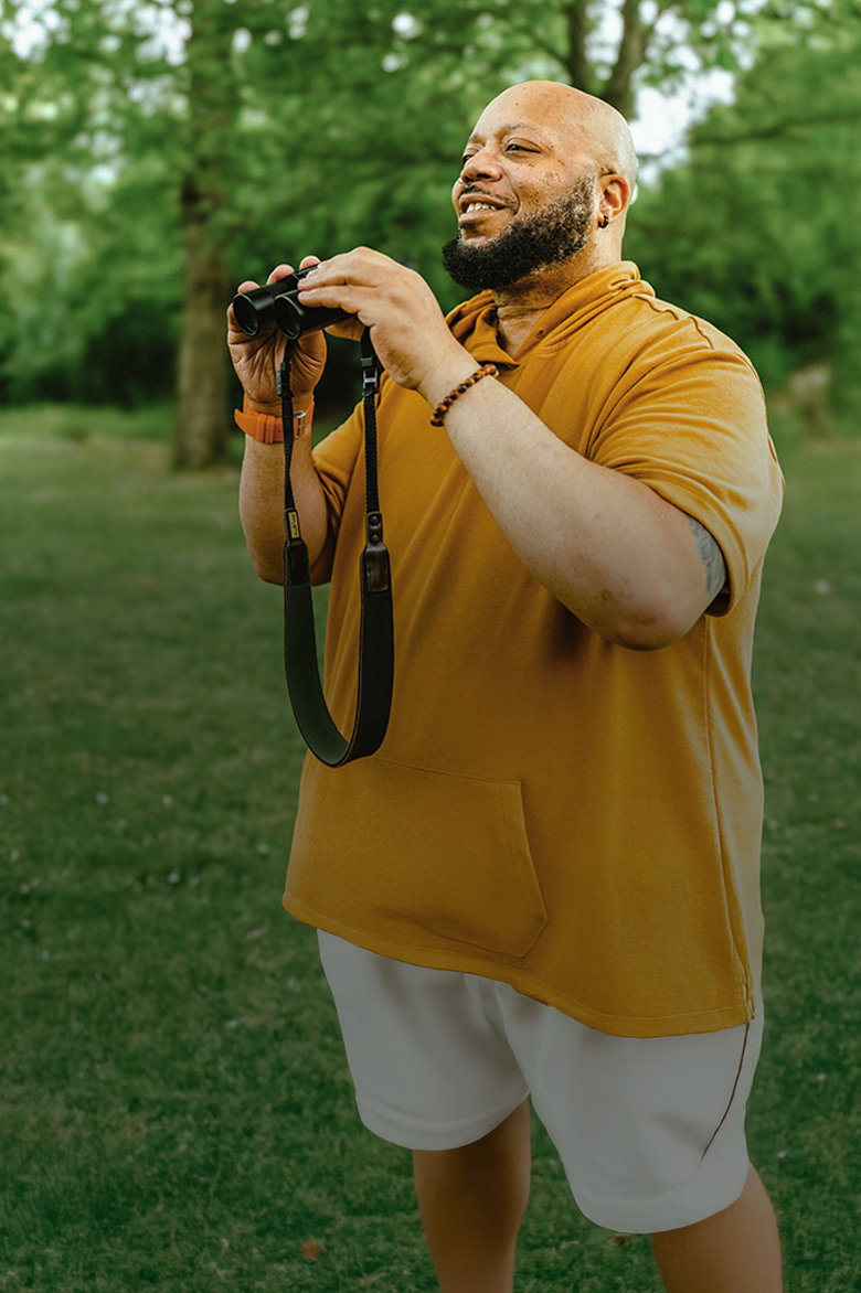 PYLARIFY Patient Al Outside Al, a PYLARIFY patient, standing outside in nature, holding binoculars