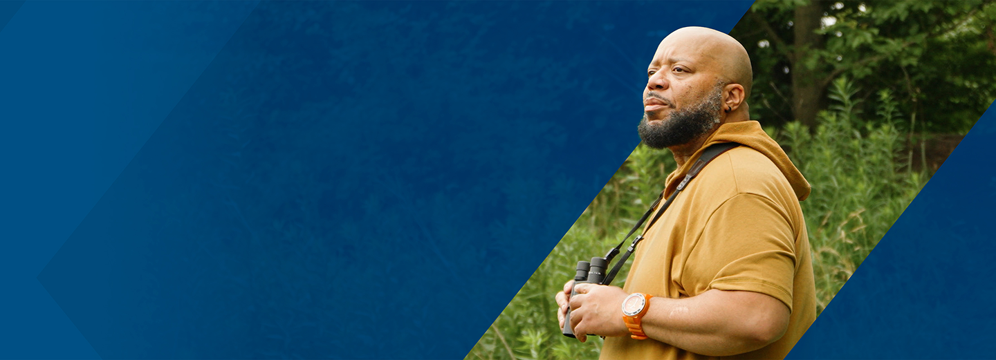 PYLARIFY Patient Al Binoculars Al, a PYLARIFY patient, standing outside in nature, holding binoculars